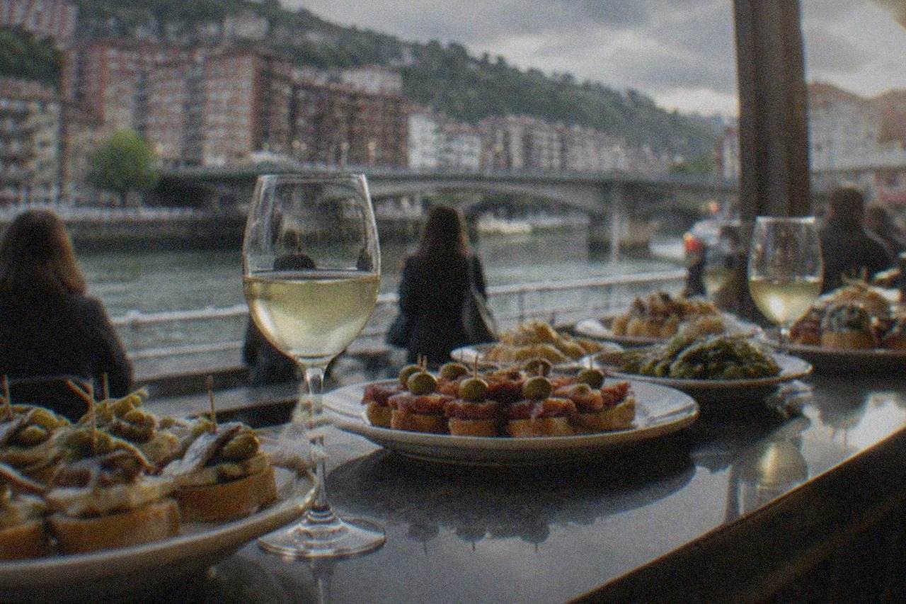 A busy pintxos bar counter in Bilbao with plates of small bites and glasses of txakoli arranged on the bar top