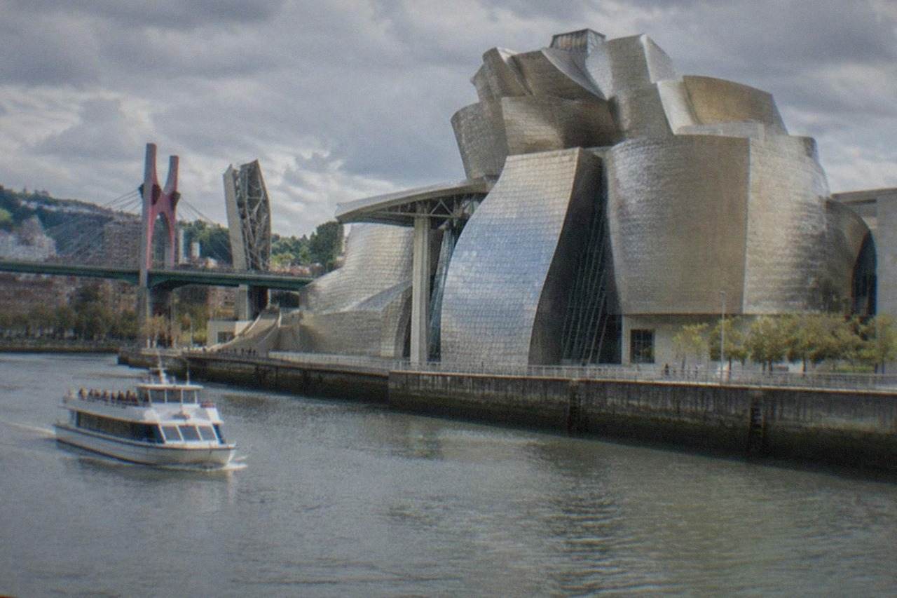 The Guggenheim Museum Bilbao beside the Nervion estuary on a bright day, with the titanium curves reflecting the sky