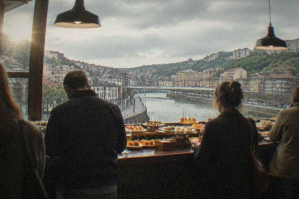 People standing at a bar in a Bilbao pintxos room, with small plates displayed on the counter