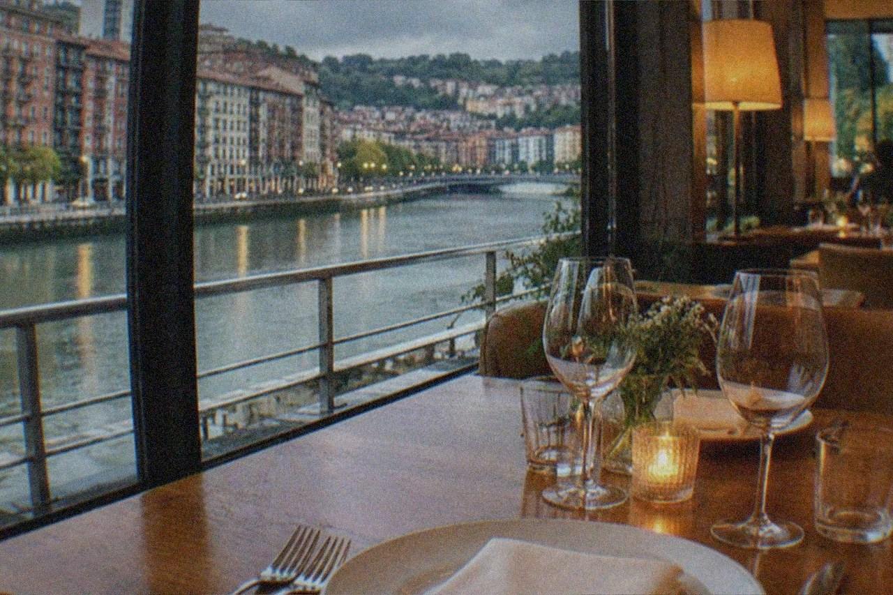 An elegant restaurant dining room in Bilbao with a set table, wine glasses and warm evening light