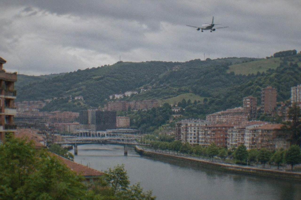 A passenger aircraft on final approach over green hills toward Bilbao Airport on a cloudy northern Spanish afternoon