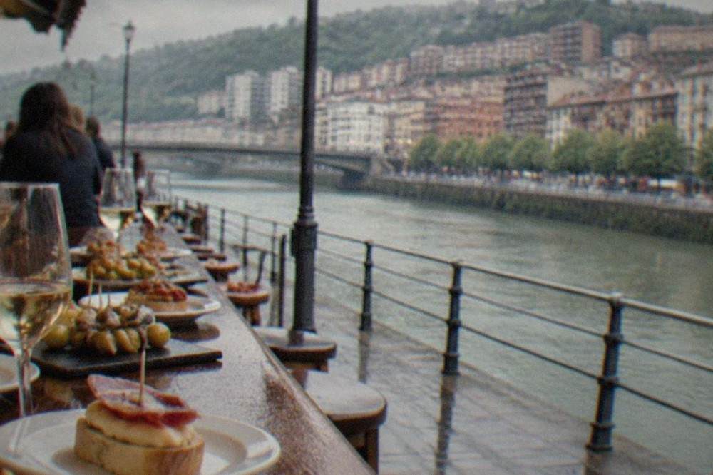 A crowded pintxos bar counter in Bilbao's old town with small plates and glasses of txakoli arranged along the bar top