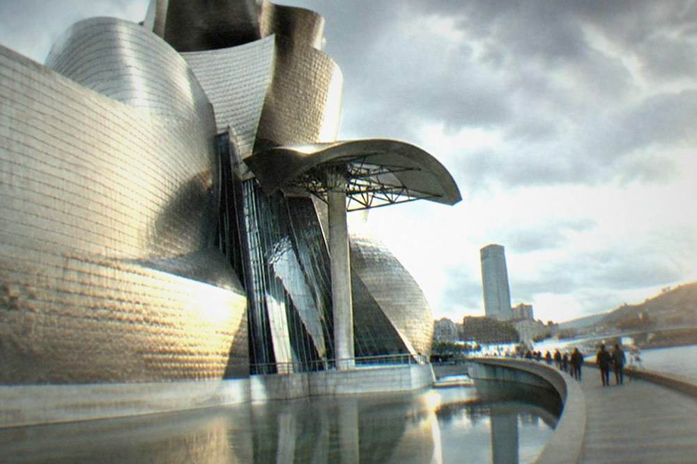 Visitors on the riverside walkway beside the Guggenheim Museum in Bilbao with the titanium curves reflected in the estuary water