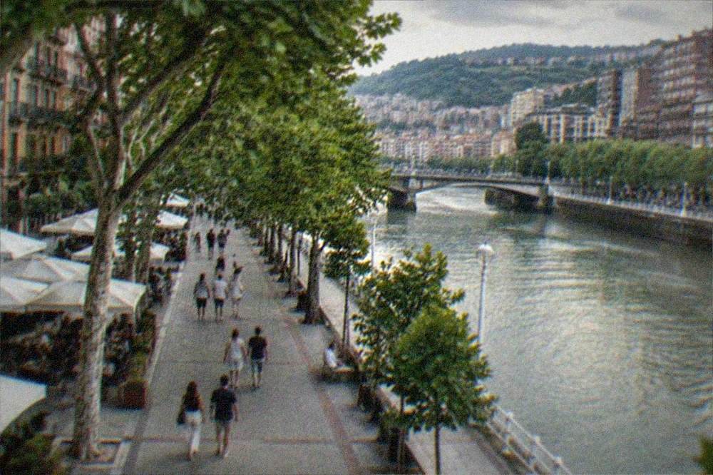 People strolling under plane trees along the Gran Vía in Bilbao on a mild summer evening with cafe terraces open