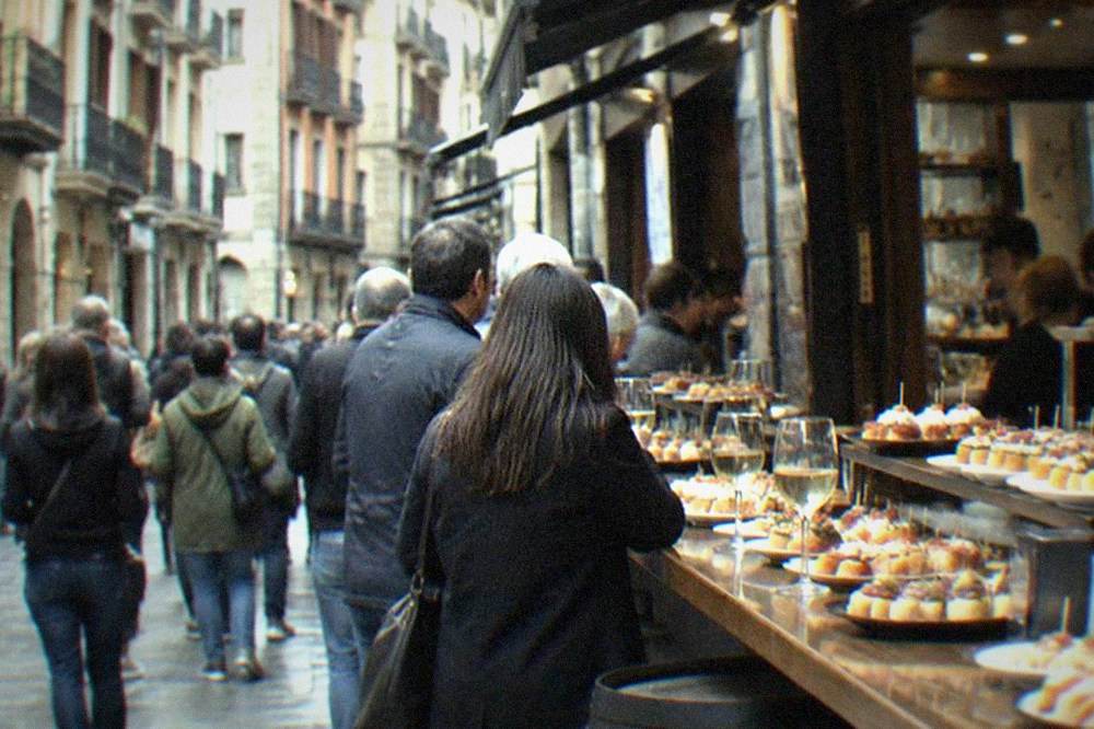Crowded pintxos bar counter in Bilbao's Old Town with plates of small bites and glasses of txakoli wine