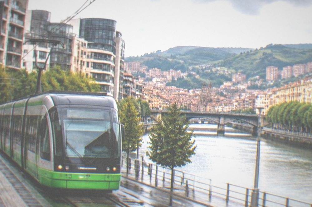 Bilbao tram passing modern buildings with the river estuary and old town rooftops beyond