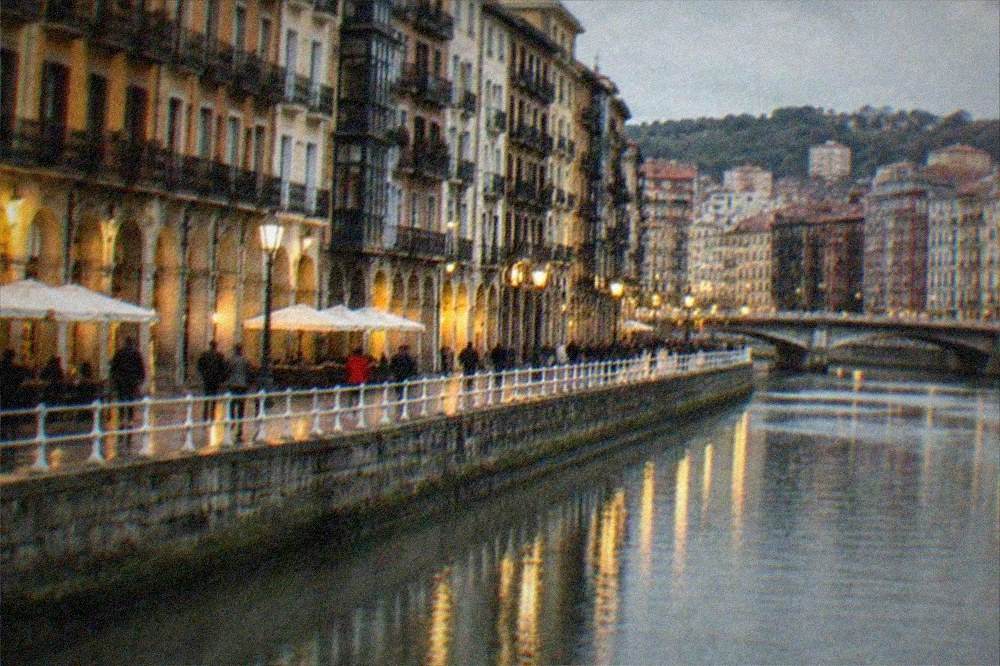 Evening view of Bilbao's old town riverside with illuminated facades and people walking along the water