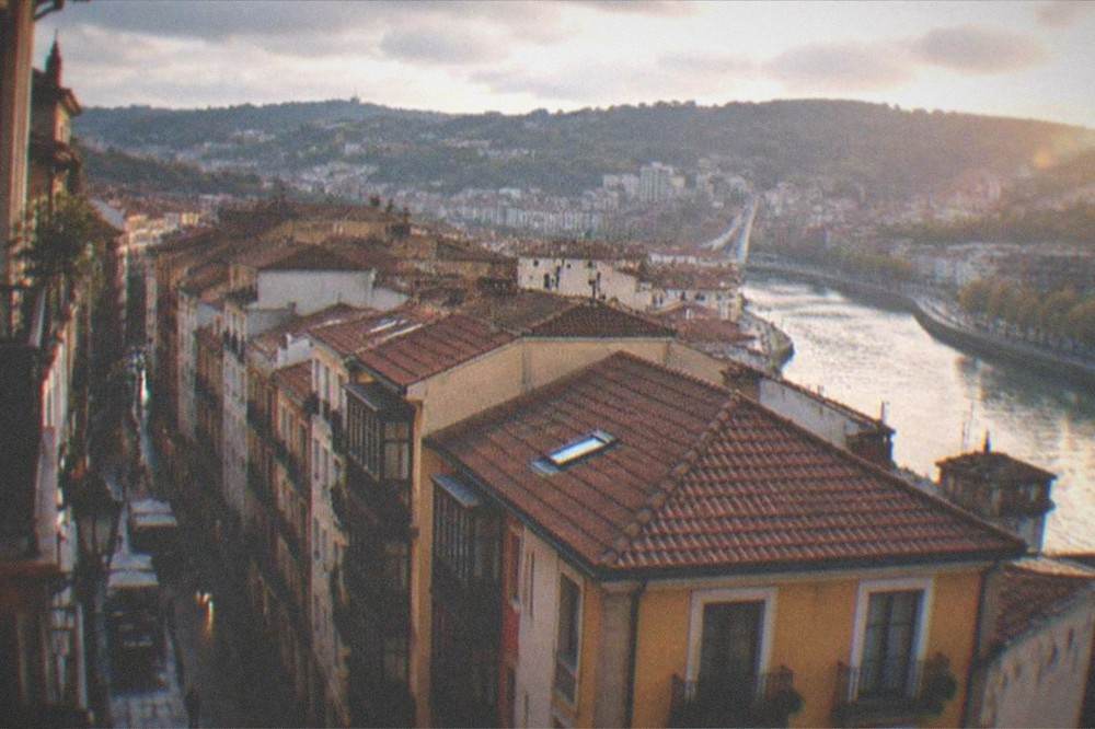 View over rooftops of Bilbao's old town toward the river with hills behind the city