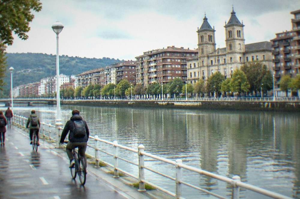 Walkers and cyclists on the Canal de Deusto towpath in Bilbao with apartment buildings behind
