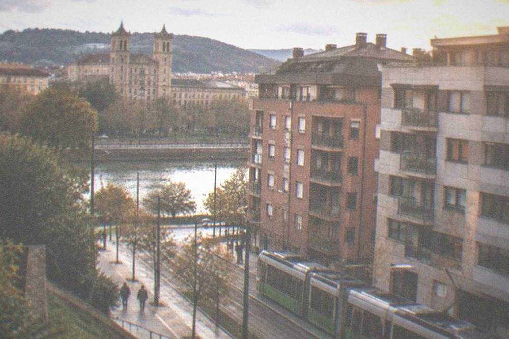 A Bilbao tram passing modern apartment buildings on a street near the Deusto district