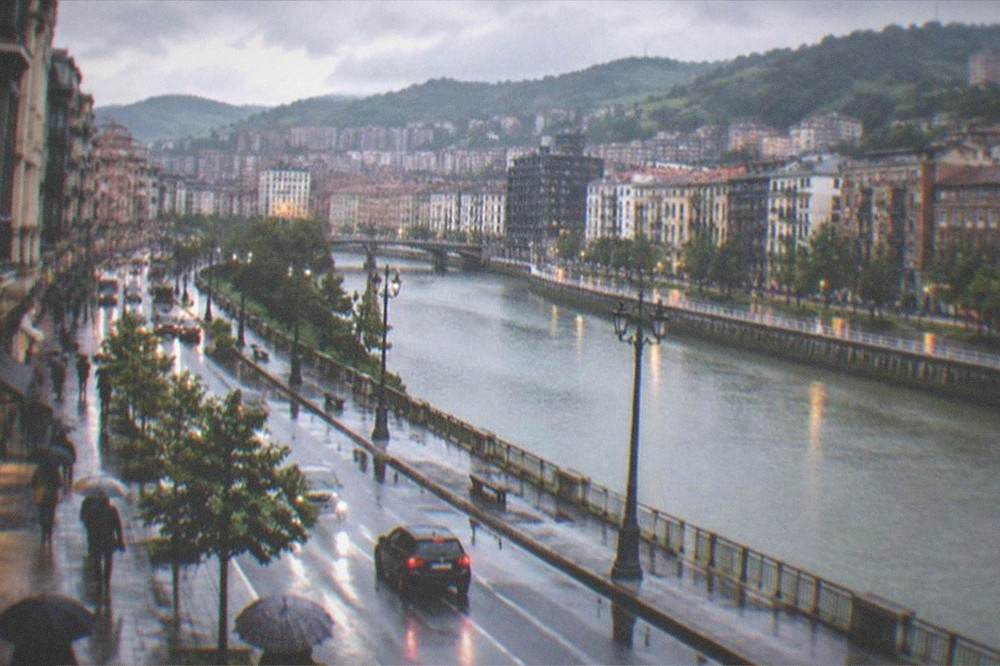 Rain-slicked pavements along Gran Via in Bilbao with umbrellas and lit shopfronts