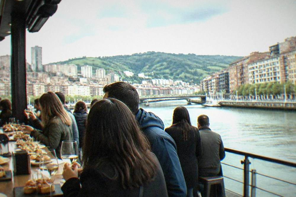 People eating pintxos and drinking wine at a crowded bar counter in Bilbao