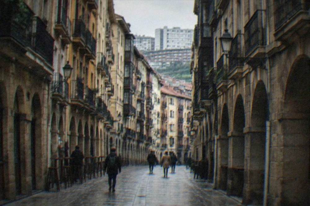 Narrow medieval street with old stone buildings in Bilbao's Casco Viejo contrasted with modern city in the background