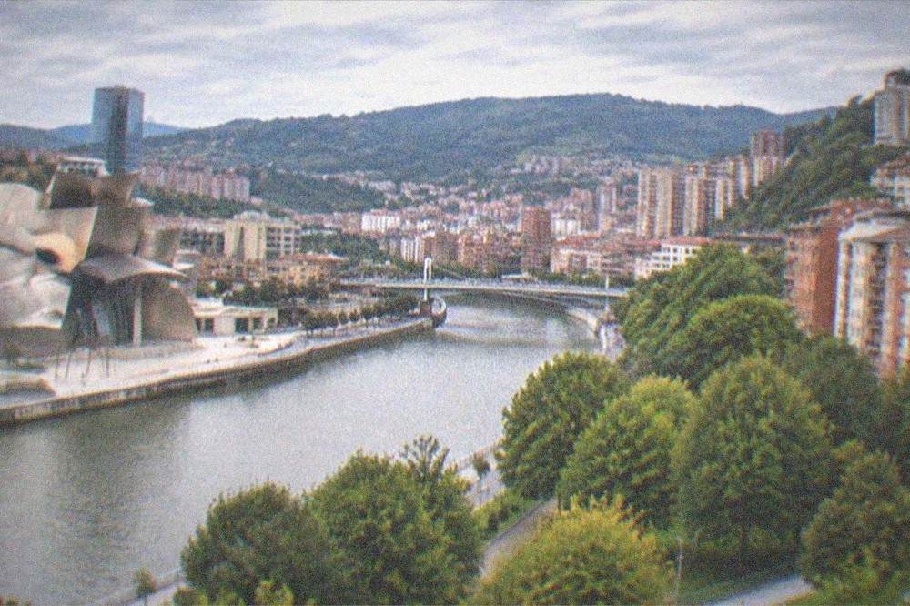 Wide view of central Bilbao at dusk with apartment buildings, green park trees and distant hills
