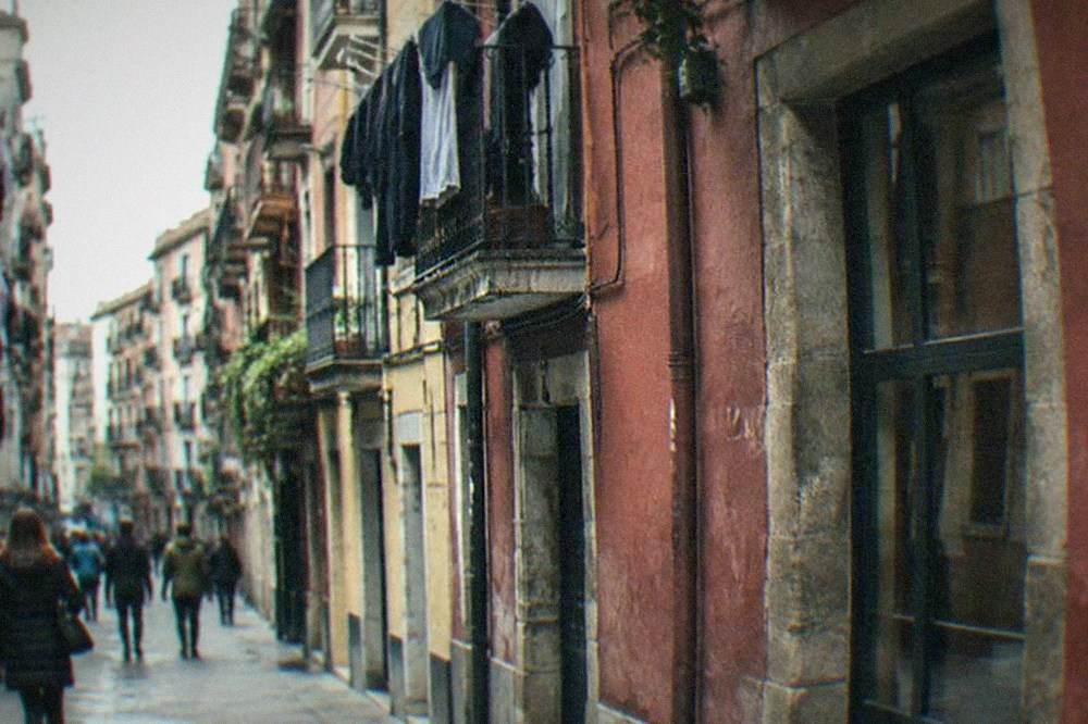 People walking past painted building facades on a narrow street with laundry hanging from balconies