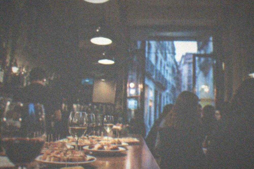 A crowded pintxos bar counter with plates of small snacks and glasses of wine