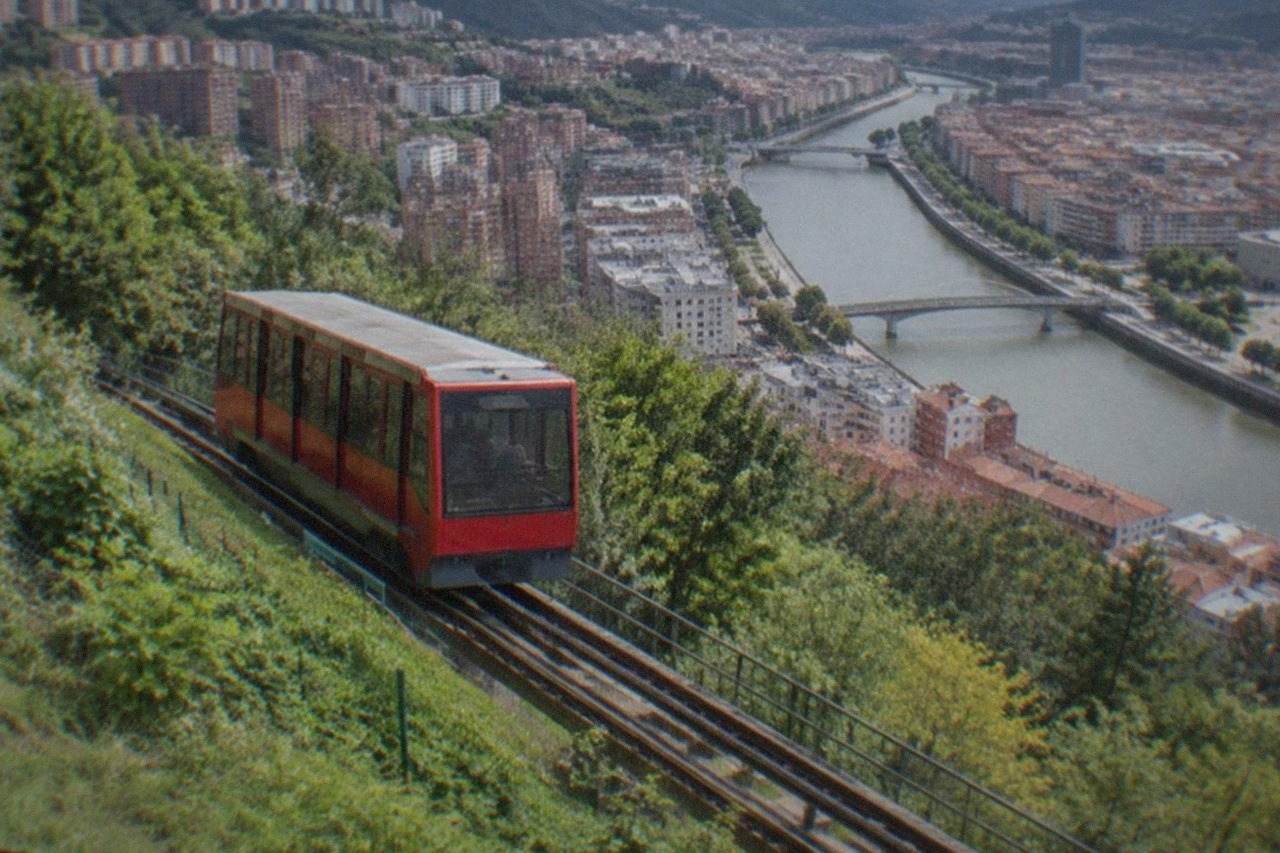 A red funicular carriage climbing the green hillside above the Bilbao city skyline