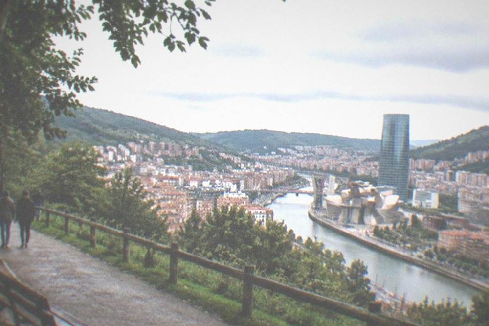 A green hilltop park path on Mount Artxanda with the Bilbao skyline in the distance