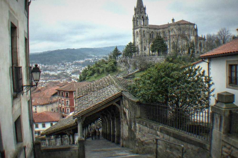 A stone staircase rising between old buildings toward a hilltop church in Bilbao