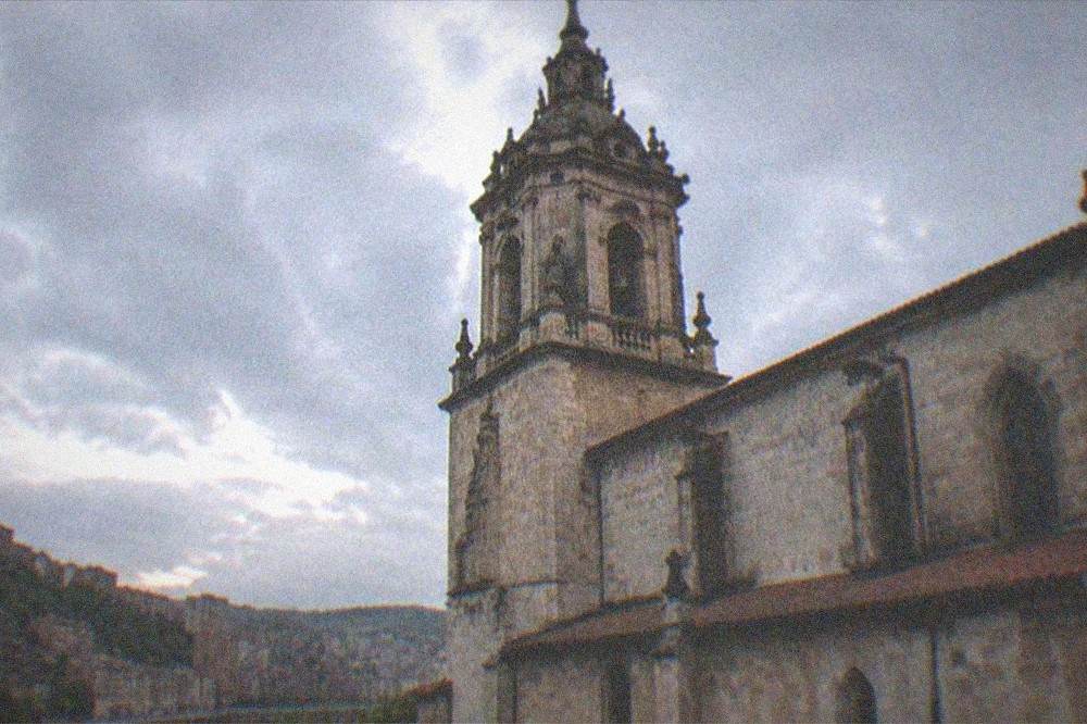 A stone basilica tower and church roof seen against the evening sky in Bilbao, Spain