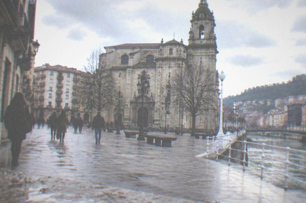 Cathedral square in Bilbao with people walking under grey skies between old buildings