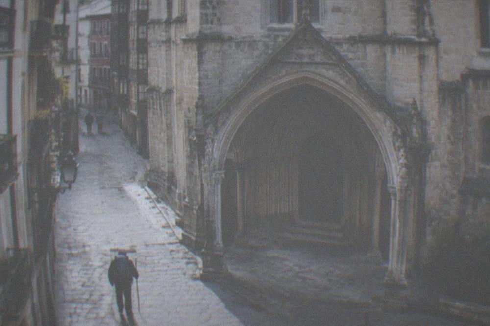 Pilgrim with a backpack and walking staff passing a gothic church in an old town street