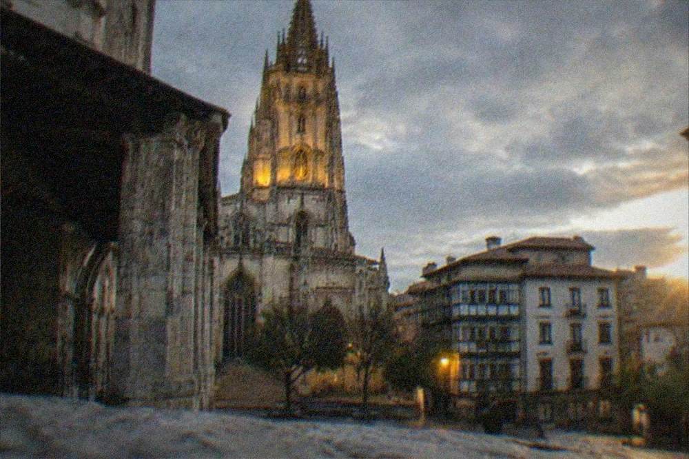 Evening view of a lit cathedral tower above the rooftops of an old Basque town