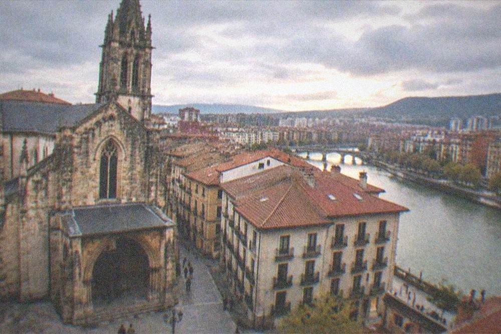 Wide view of a Basque city old town with a gothic tower and a river beyond at dusk