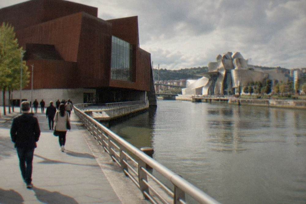 Visitors walking along the riverside promenade toward Euskalduna Palace with the Guggenheim Museum visible in the background