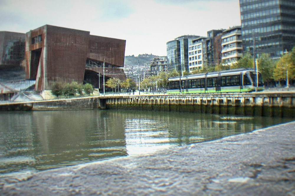 A tram passing modern buildings on the Abandoibarra waterfront in Bilbao near Euskalduna Palace