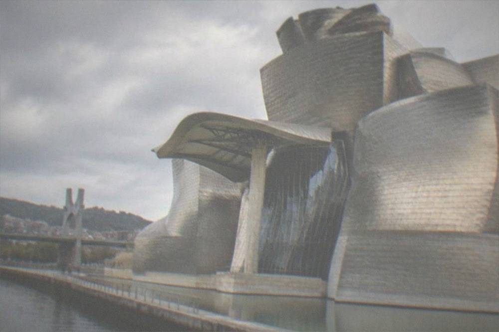The curved titanium exterior of the Guggenheim Museum seen from the riverside walk near Euskalduna Palace