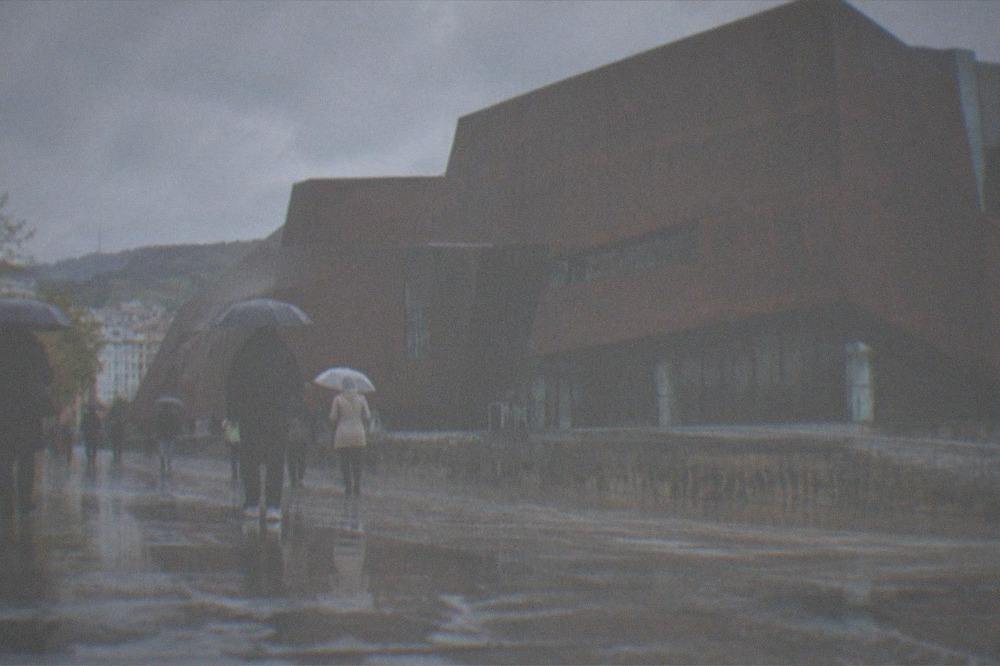 People with umbrellas walking past Euskalduna Palace in Bilbao during light rain