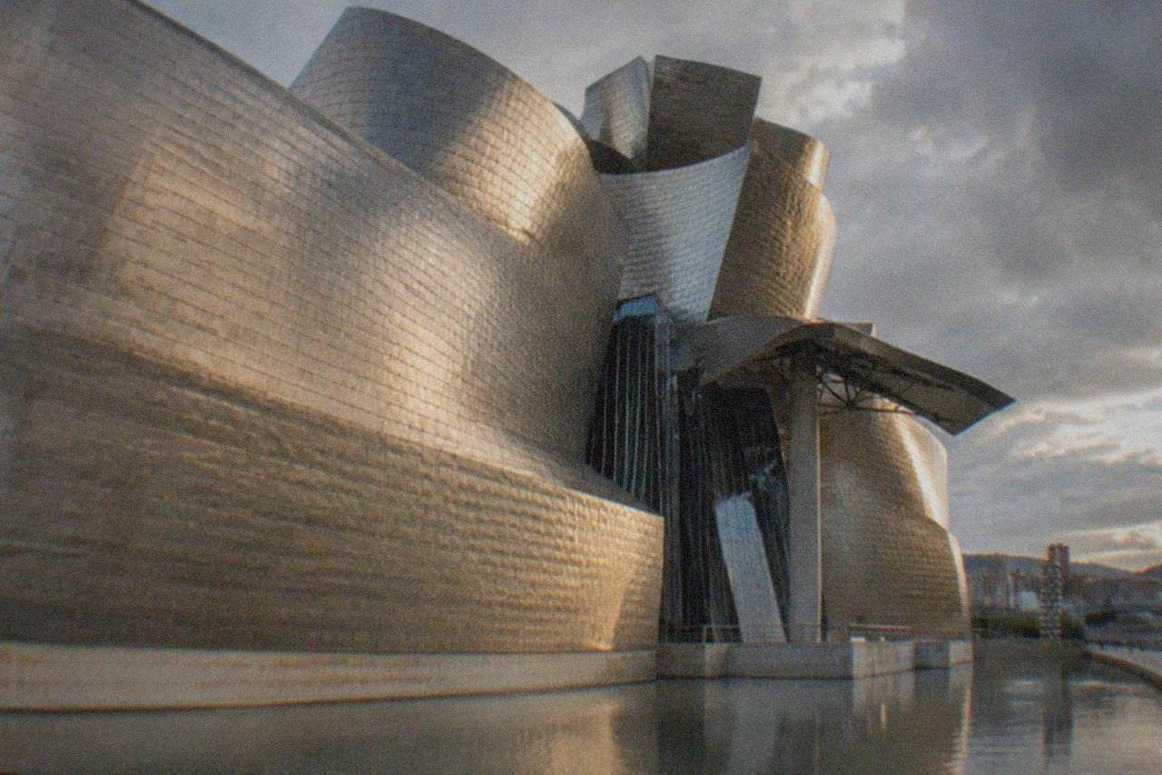 The curved titanium exterior of the Guggenheim Museum Bilbao beside the water on a clear day