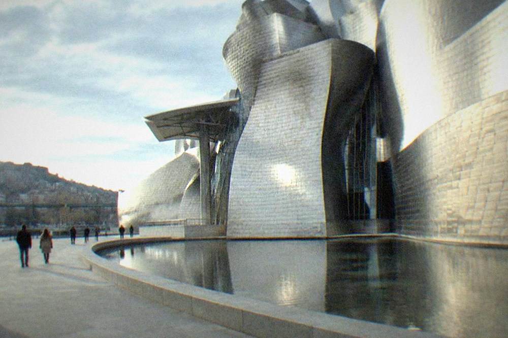 A wide plaza beside the museum with people strolling and the building's reflective panels catching afternoon light