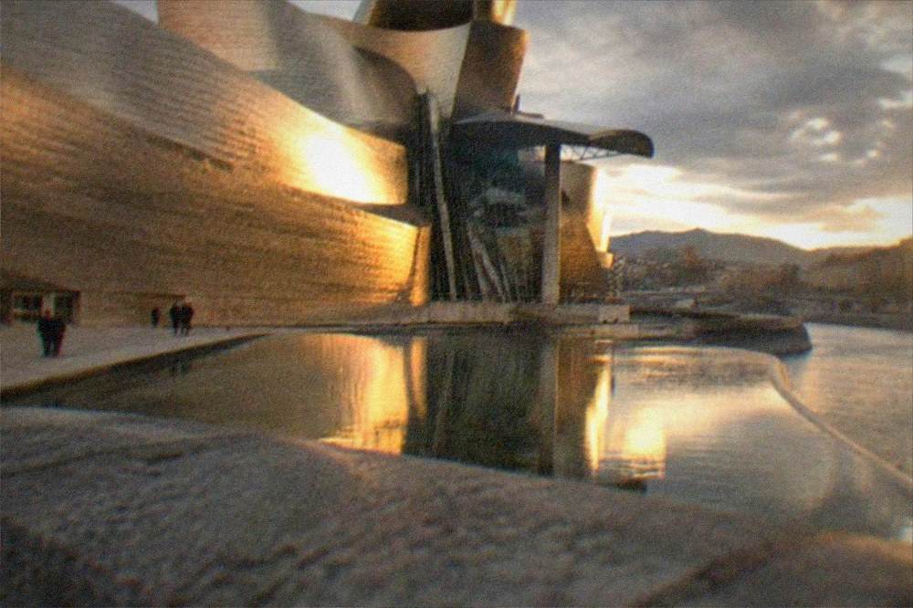 The museum's titanium panels glowing warm orange in late afternoon light beside the river