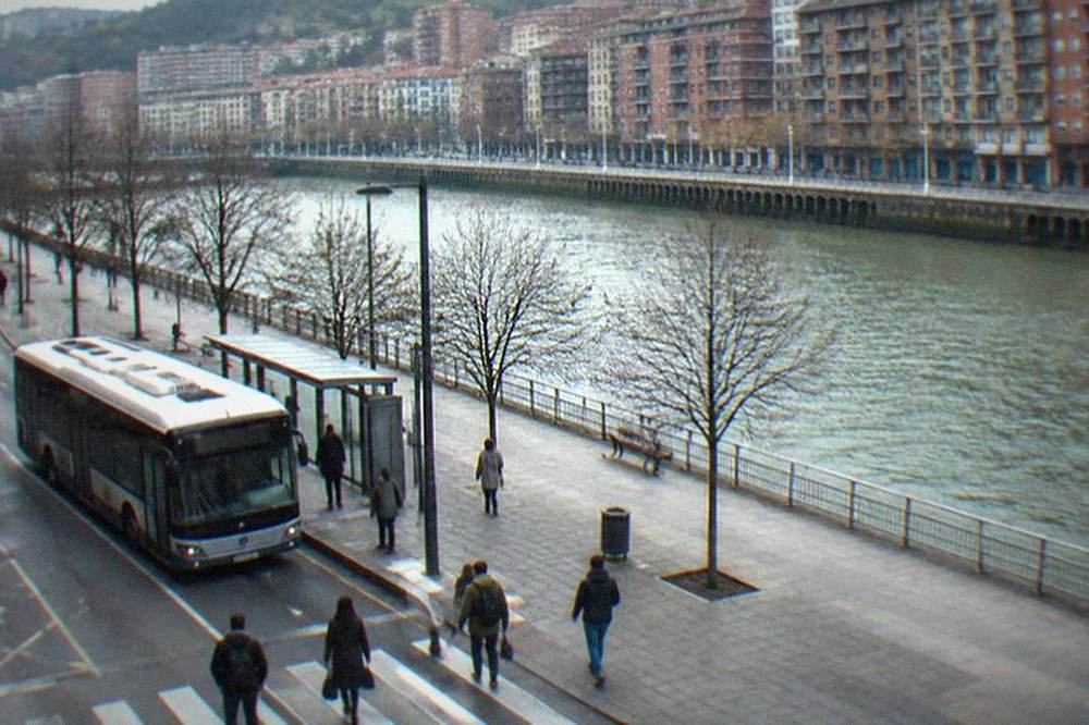 A Bilbao street with a low-floor city bus at a stop and pedestrians crossing