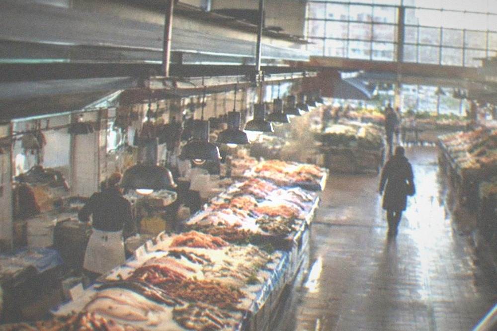 A covered market aisle with a fishmonger counter and hanging lights in the morning