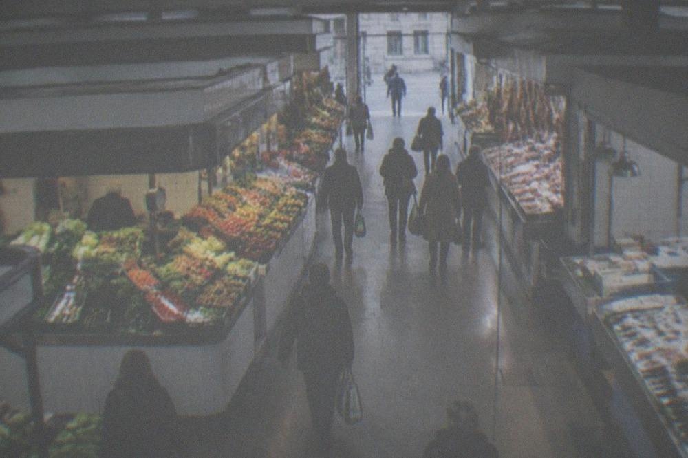Shoppers walking past market stalls toward a bright street entrance