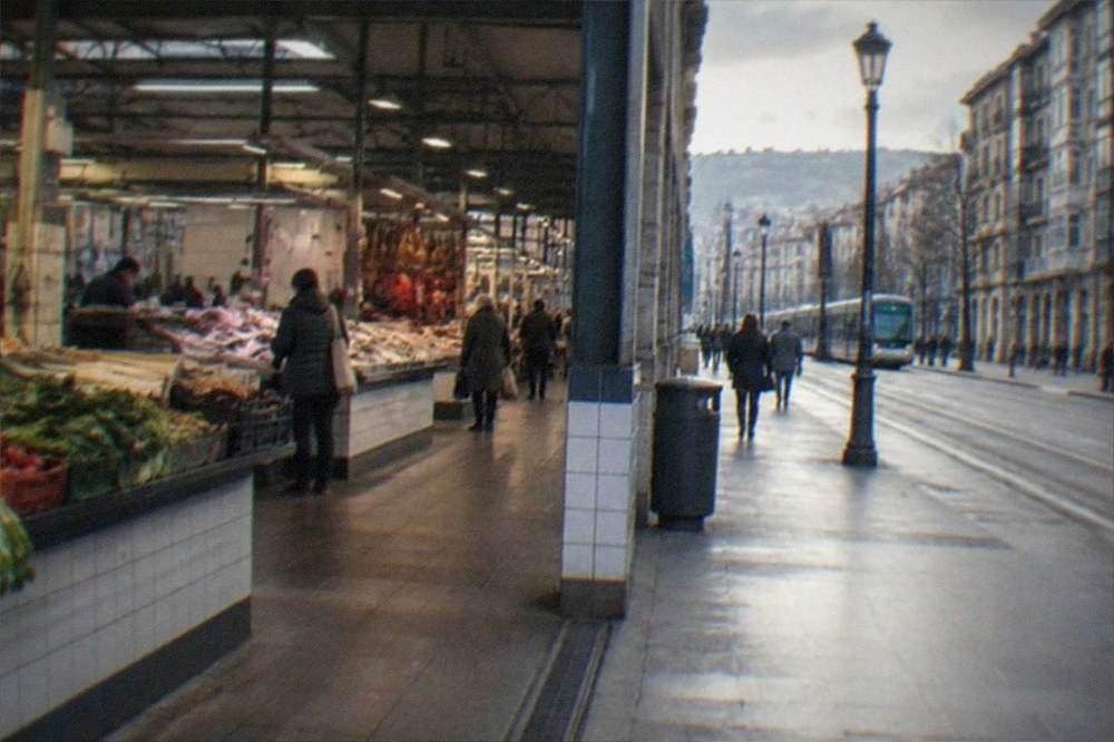 A city avenue with pedestrians, tram tracks and stone buildings under a soft sky