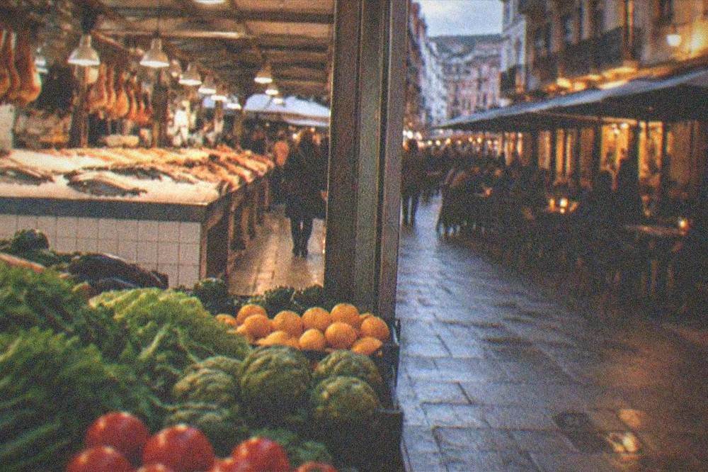 Evening view of a market street with lit bar fronts and people gathered at outdoor tables
