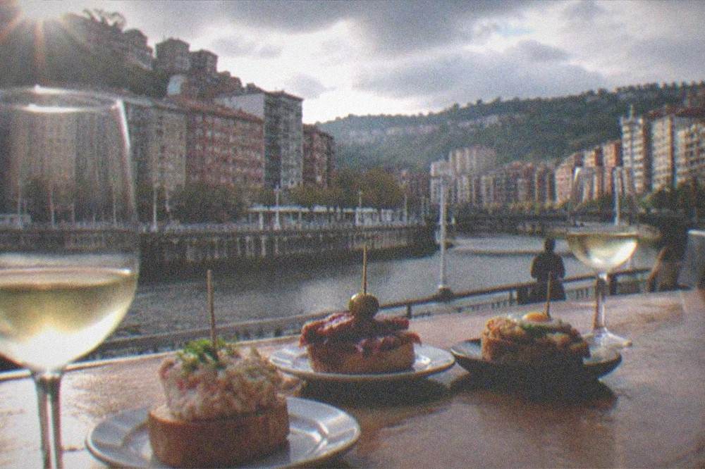 Pintxos and glasses of txakoli arranged on a wooden bar counter in Bilbao