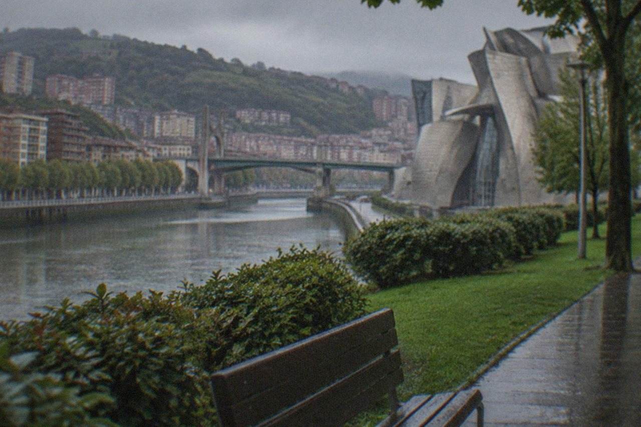 Tree-lined path and green lawns of a city park beside a museum building in Bilbao