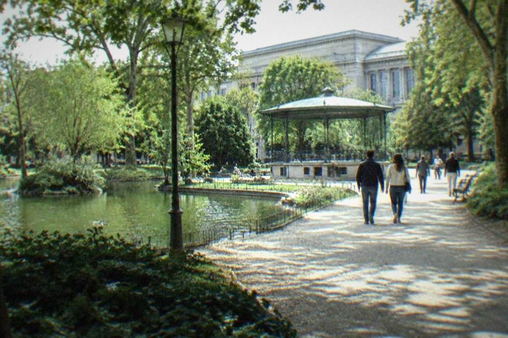 Visitors walking along a park path with a large museum facade visible beyond the trees