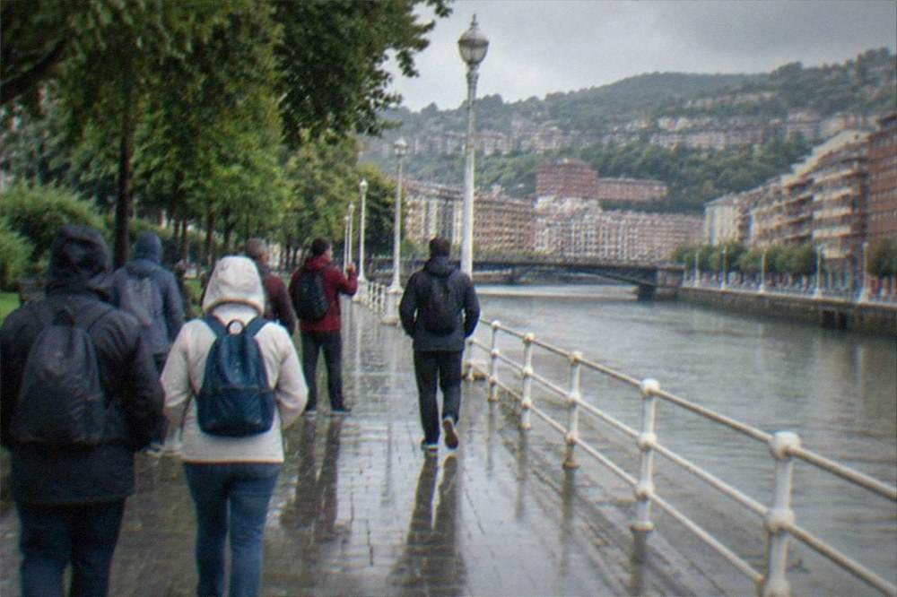 A guided walking group pausing on a boulevard near a park entrance in Bilbao