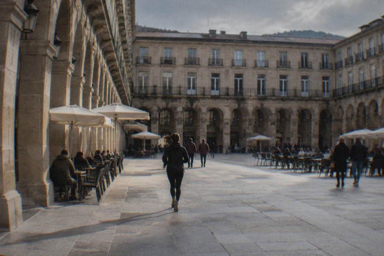 Arcaded neoclassical square in Bilbao's old town with outdoor tables and people walking under stone arches