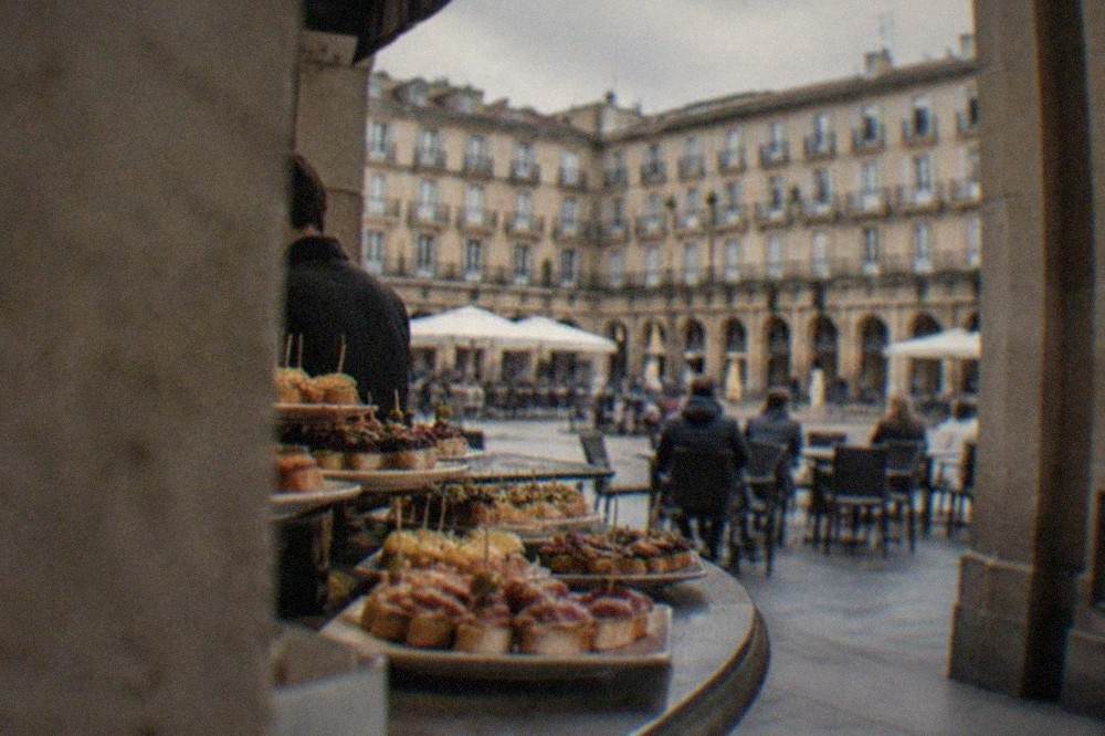 Close view of pintxos displayed on a bar counter under the arcades of a stone square
