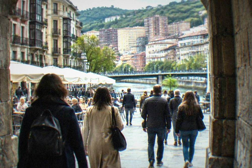 People walking through a stone archway into a lively square with cafe tables in Bilbao