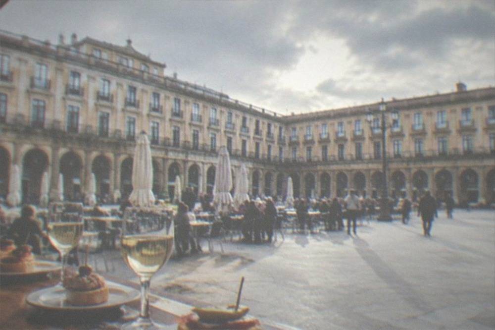 Small glasses of txakoli wine and pintxos on a wooden bar counter in a crowded tavern