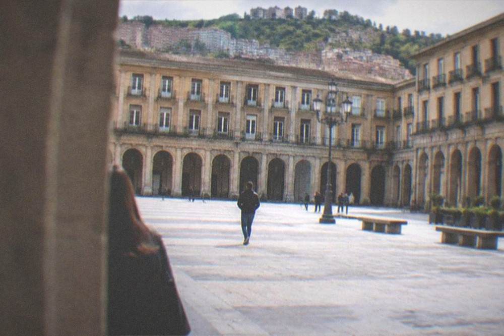 Wide daytime view of a neoclassical square with uniform stone arches on all four sides in Bilbao