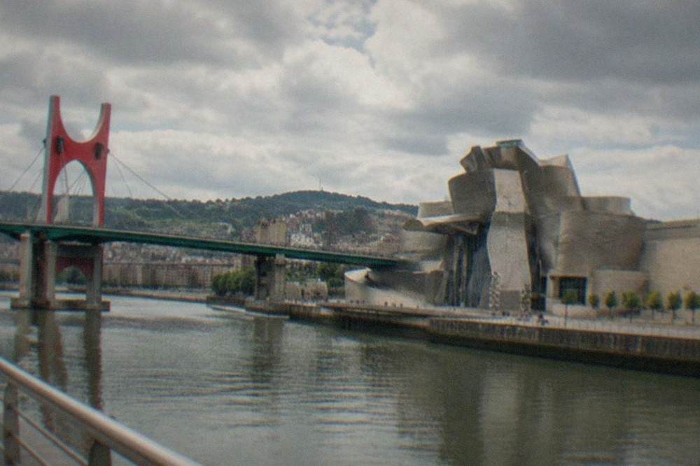 View from a bridge platform over a city river with a curved metallic museum building on the bank